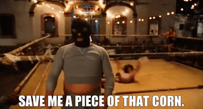 A person wearing a balaclava and a hoodie stands in front of a wrestling ring with the caption "SAVE ME A PIECE OF THAT CORN."