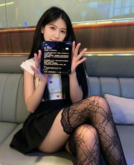 A young woman with long black hair sits on a couch holding up a phone displaying text, dressed in a white polka-dot top, black skirt, and lace stockings, seemingly presenting a message of apology addressed to "Teacher Jin" related to Binance.