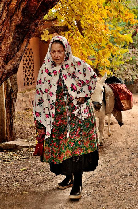 An elderly woman in a floral headscarf and patterned dress walks along a dirt path, led by a donkey carrying sacks. The image captures a quiet morning scene that reflects the peaceful, early start suggested by the post's "Good Morning" greeting.