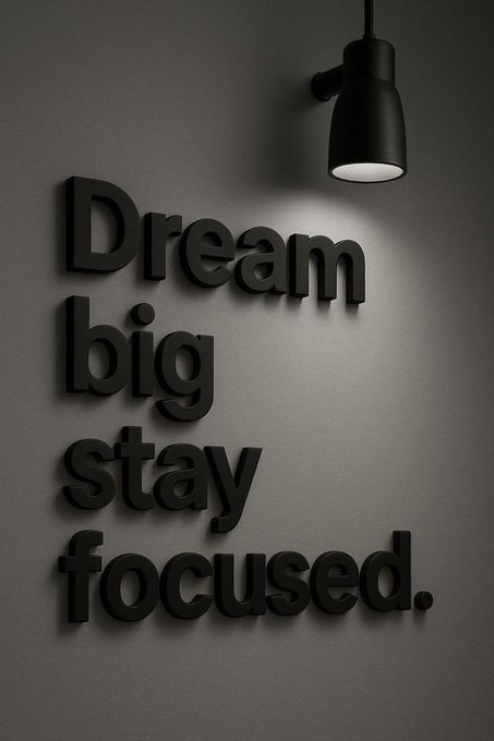 Black 3D wall art spelling 'Dream big stay focused.' illuminated by a single black spotlight fixture mounted on a gray wall.