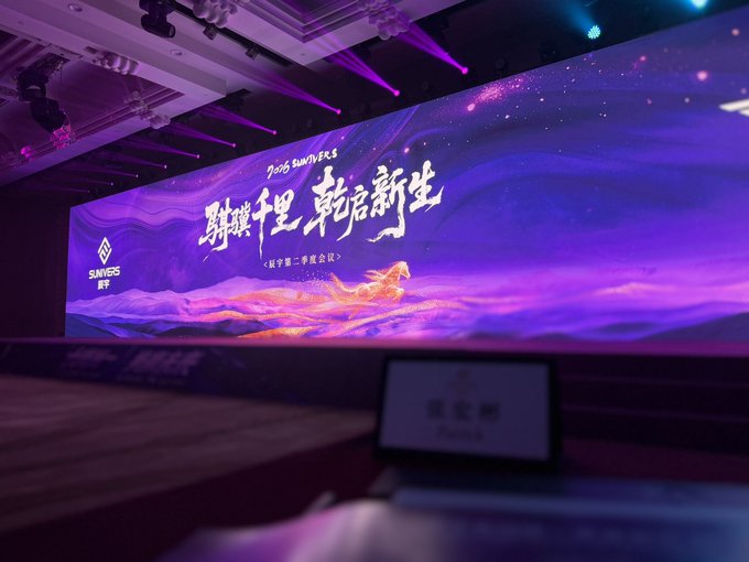 An indoor event stage with a large illuminated screen displaying '2025 SUNING' branding and Chinese text '聚耀千里 革启新生' (gathering glory for a thousand miles, revolutionizing new life) with a galloping horse graphic, lit in purple and blue.