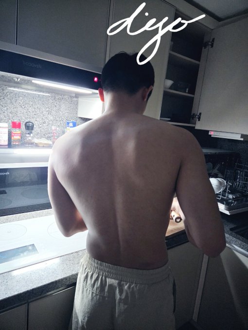 A shirtless man stands in a kitchen facing away from the camera to showcase his back muscles, with the name "digo" written in white script at the top of the image, directly tying into the post introducing "Digo's back gains" and his fitness routine.