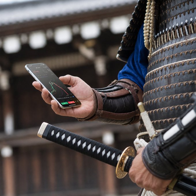 A samurai in traditional armor examines a trading chart on his smartphone while gripping his katana, embodying the discipline of waiting for the perfect moment to strike—whether in battle or the markets.