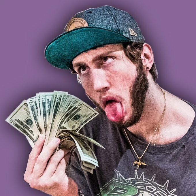 A photo of a young man with a beard wearing a cap, sticking his tongue out while holding a fan of US dollar bills against a purple background.
