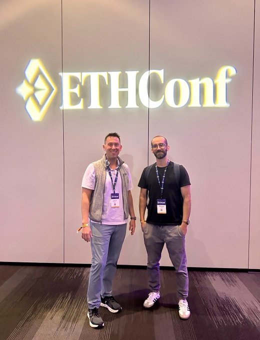 Two attendees pose in front of the illuminated "ETHConf" sign while wearing lanyards, representing TRON DAO's participation at the Ethereum conference where they launched the HackaTRON Global Hackathon with a million-dollar ecosystem fund.