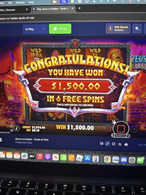 A laptop screen displays a slot machine game called "Zeus vs Hades - Gods of War" showing a "CONGRATULATIONS YOU HAVE WON $1,500.00 IN 6 FREE SPINS" screen with a credit balance of $1,914.46 and bet of $0.10, aligning with the post's celebration of a max win at @rainbetcom. The macOS dock and keyboard are visible at the bottom of the image.