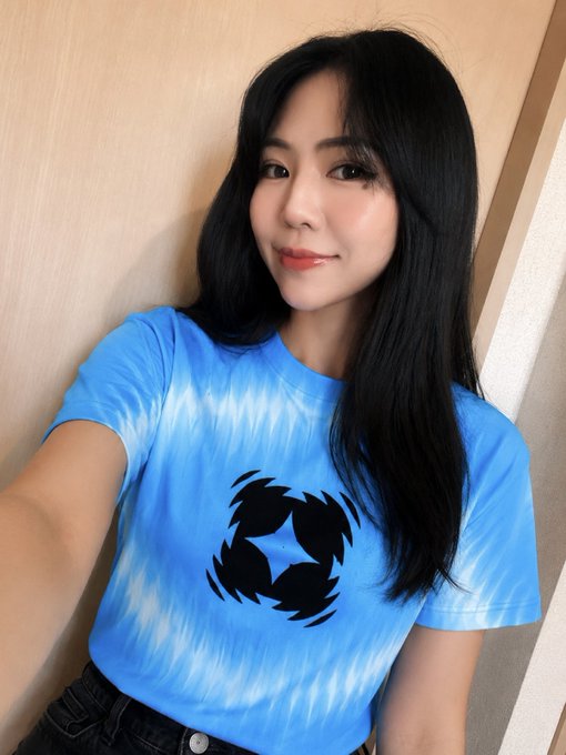 The image features a woman wearing a blue tie-dye shirt with black designs, including a skull or a circle pattern. The woman appears to be posing for a photo, possibly sharing her outfit choice with others through social media platforms like Twitter.