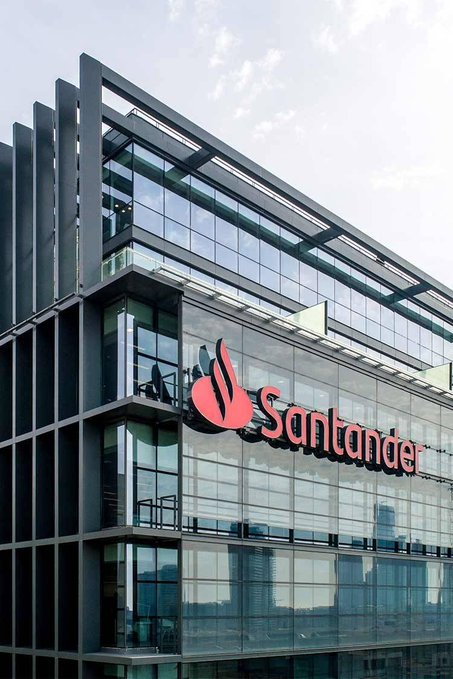 A modern glass building prominently displays the red "Santander" logo and emblem, representing the European banking giant that has reportedly purchased $12 million in Bitcoin for its balance sheet, marking a significant milestone in institutional cryptocurrency adoption.