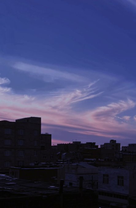 A twilight sky with pink and purple wispy clouds hangs over the silhouettes of city buildings.