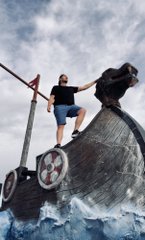A blurry image captures two figures in traditional attire pulling ropes on a boat or structure over water, with motion blur suggesting rapid movement.