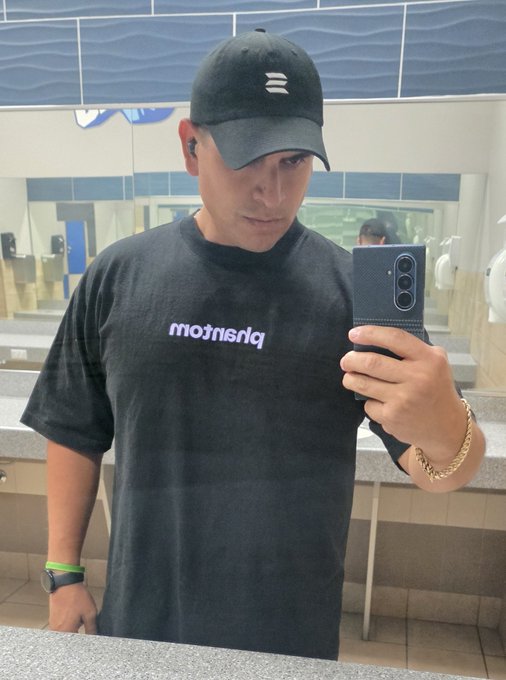 A man wearing a black "balenciaga" t-shirt and cap takes a mirror selfie with his phone in a public restroom, accompanied by the caption "Unemployed but still locked in on solana"—suggesting his commitment to the Solana blockchain despite being jobless.