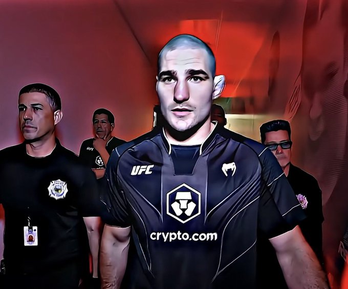 A stylized image of a UFC fighter in a black 'crypto.com' walkout shirt being escorted through a tunnel by officials in dark uniforms.