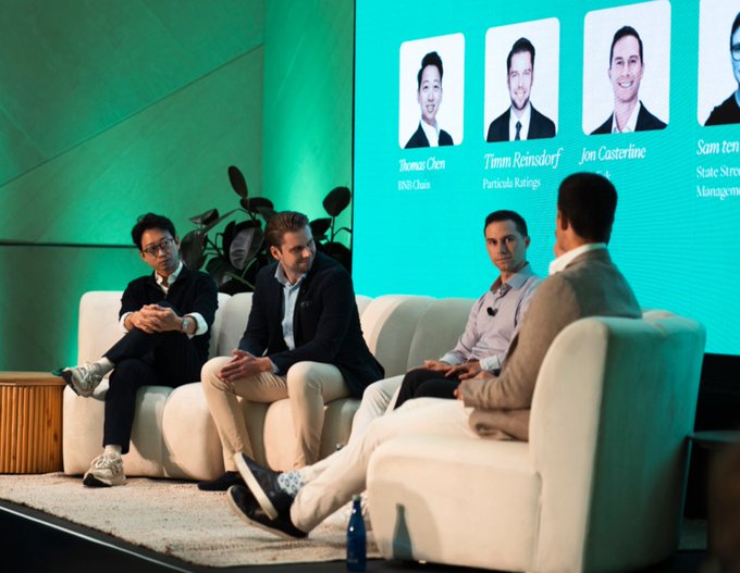 A panel discussion at the RWA Summit features Thomas Chen of BNB Chain alongside Timm Reinisdorf of Particula Ratings, Jon Castorino, and Sam ter Stehn of State Street Management, seated on white couches while their names and affiliations are displayed on a large screen behind them, illustrating Chen's insights on real-world assets and BNB Chain's role in connecting RWAs to global investors.