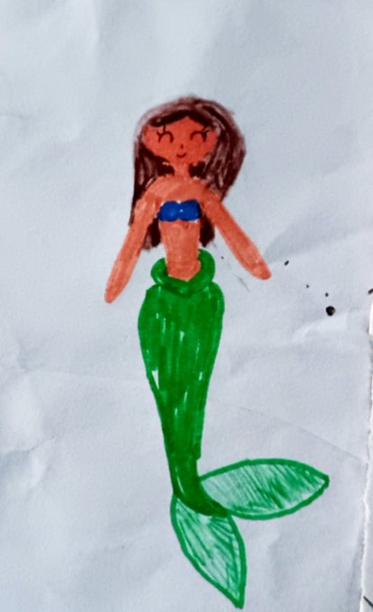 A child's drawing on white paper shows a mermaid with brown hair, a blue top, and a green tail.