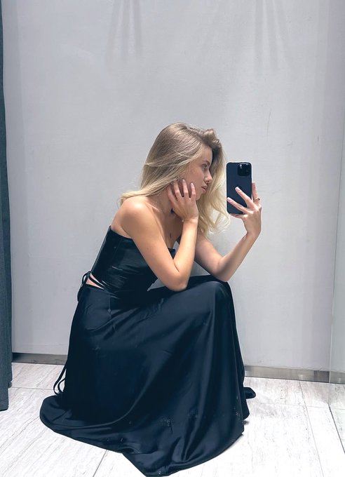 The image features a woman sitting down, looking at herself in a mirror with her reflection visible. The photo has been captioned "$BTC always brings us many different surprises! Do you think it's a bull market or a bear market now?". This suggests that there might be some speculation or discussion about the current state of the cryptocurrency market and its potential impact on various aspects, including fashion trends like the one depicted in the image.