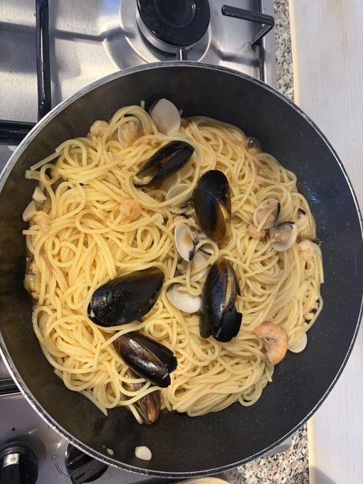 A pan of spaghetti with mussels and clams on a gas stove, a seafood pasta dish ready to be served.