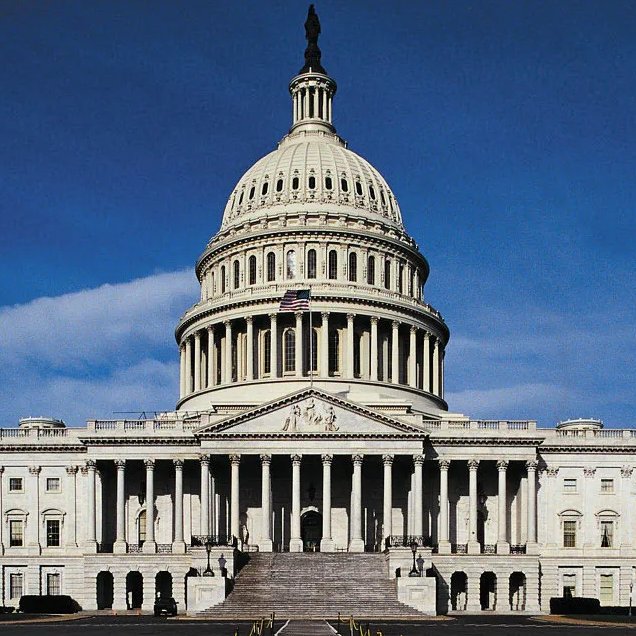 A photograph of the United States Capitol Building showing its iconic white dome and neoclassical facade against a deep blue sky with an American flag flying in front.