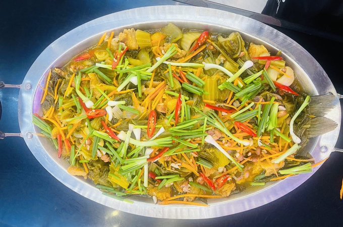 A large oval metal platter filled with a whole cooked fish topped with colorful julienned vegetables, including green onions, carrots, and red peppers.