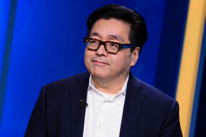 A man with dark hair and tortoiseshell glasses, wearing a dark blazer over a white shirt, is shown against a blue background in what appears to be a television studio setting. The image likely depicts Tom Lee, the Fundstrat analyst mentioned in the post about BitMine's substantial $71.6 million Ethereum purchase through FalconX and Kraken exchanges.