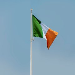 The image shows the flag of Ireland—green, white, and orange—waving against a clear blue sky. It visually accompanies the post about Ireland's Criminal Assets Bureau addressing organized crime's use of private vaults to hide crypto seed phrases and private keys.