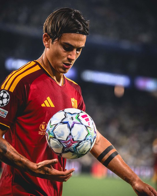 A Roma player in a maroon and yellow kit looks down at a UEFA Champions League-style starball during a match, with the "World Food Programme" sponsor and adidas logo visible on his jersey, tying into the post about a high-stakes betting win on the Roma vs. Fenerbahce draw.