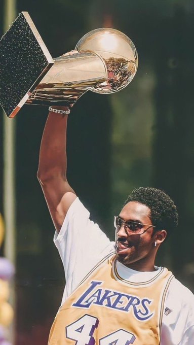 A basketball player wearing a Lakers jersey with the number 44 holds up a championship trophy.