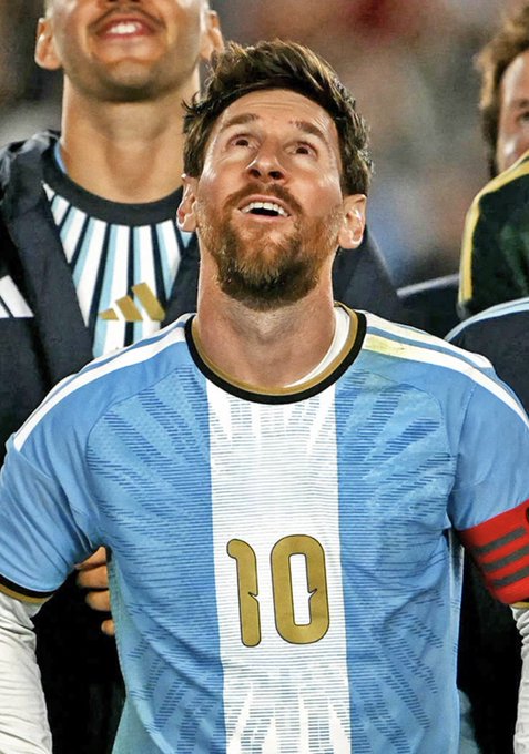 Soccer player Lionel Messi, wearing an Argentina national team jersey with the number 10, looks upward during what appears to be a national anthem moment.