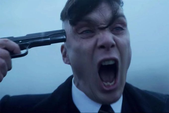 A dramatic cinematic still showing a man in a suit screaming while pressing the barrel of a gun against his own temple, with a cloudy sky in the background.