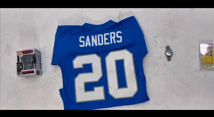 The image features a blue t-shirt with the number "20" displayed, likely representing the name of a sports team or player. There are also two other items present in the scene - a watch and a toy figurine. The objects appear to be casually placed on a table or countertop, suggesting that they might have been collected as memorabilia or used for display purposes.