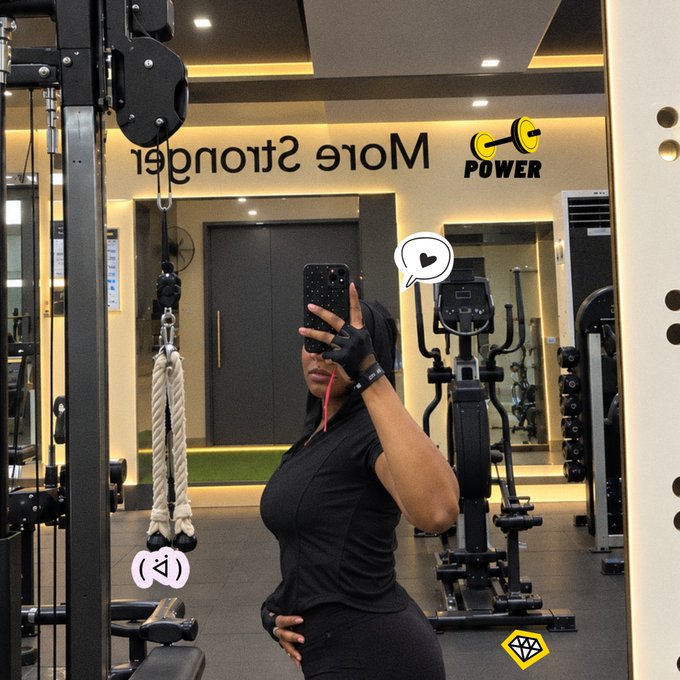 A woman in black athletic wear takes a mirror selfie in a gym with 'Mole Stronger' signage visible (shown reversed) along with a 'POWER' logo featuring a barbell icon.