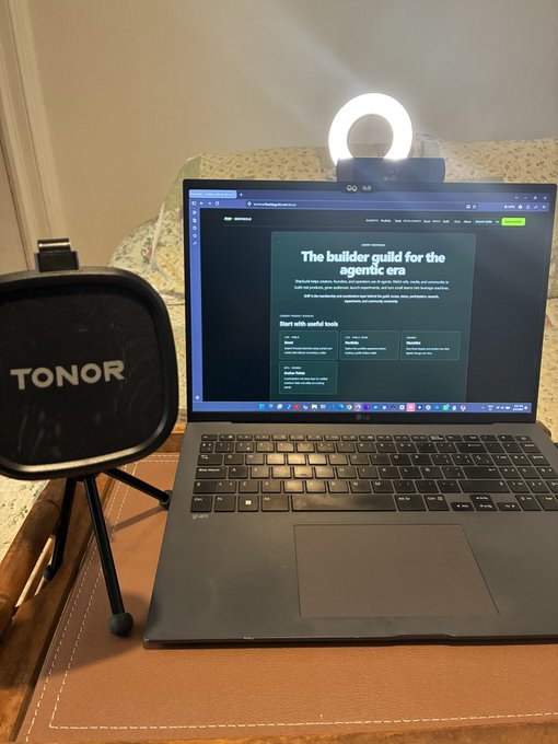 A laptop displays a webpage titled "The builder guild for the agentic era" while a TONOR microphone and ring light are set up beside it, ready for a portable livestream setup.