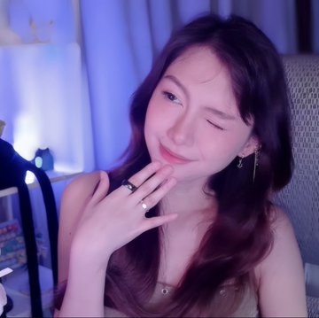 A young woman winks playfully at the camera while resting her hand near her chin, prominently displaying a sleek black ring on her finger that matches the @Tangem ring she's showcasing. The soft blue lighting creates a cozy, intimate vibe as she greets followers with a "gm" in anticipation of her upcoming video.