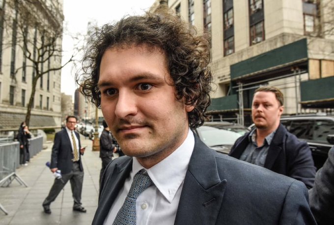 𝗝𝗨𝗦𝗧 𝗜𝗡: FTX founder Sam Bankman-Fried, who was once a convict, has been overturned by overturning his conviction and prison sentence. The image shows him posing for a picture with two men in suits standing behind him on the sidewalk.