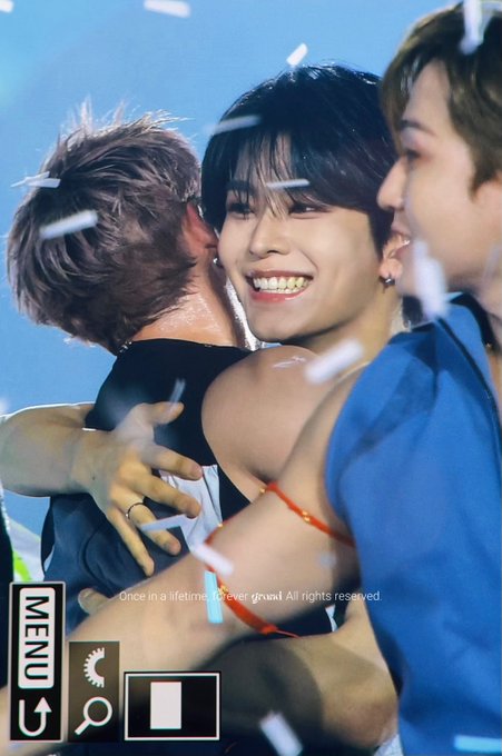 Photo of three men embracing on stage with confetti falling, with text 'Once in a lifetime, forever proud. All rights reserved.' and menu icons overlaid.