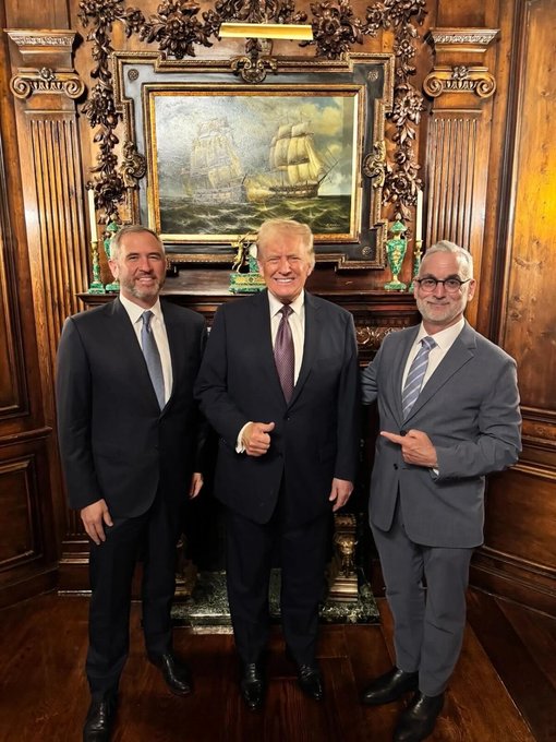 Three men in business suits stand smiling in a wood-paneled room featuring an ornate fireplace, above which hangs a large framed painting of tall ships at sea. The post appears to reference Brad Garlinghouse (@bgarlinghouse), Ripple's CEO, who is likely the bearded man on the left, posing alongside President Donald Trump in the center.