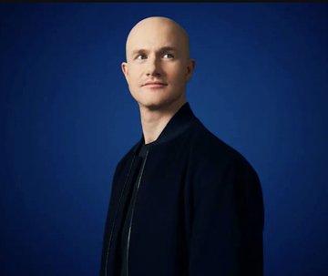 A studio portrait of a bald man wearing a dark navy jacket against a blue gradient background, looking confidently at the camera.