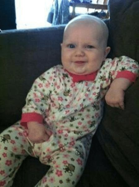 A smiling baby in floral pajamas lounges contentedly on a couch. The image humorously contrasts the stock market's seasonal strength cycles (with July being strong and later months showing red candles) to the pure, uncaring joy of infancy.