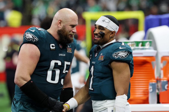 Two Philadelphia Eagles football players in dark green jerseys, numbers 62 and 1, shaking hands and smiling on the sidelines during a game.