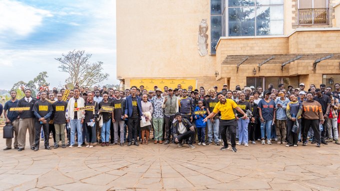 A diverse crowd poses together outside a stone building during the Binance in Your City event in Nyeri, with attendees wearing branded shirts reading "BINANCE IN YOUR CITY" and "BINANCE ANGELS," reflecting the community gathering described in the post.
