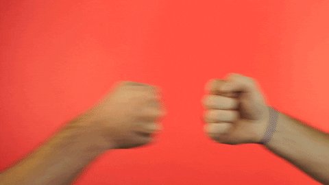 The image shows two hands making fists, with their knuckles pointing towards each other as if they are about to punch one another. The background of the image is a solid red color, which contrasts sharply with the white text that appears to be part of the photo caption.