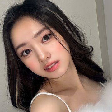 A close-up selfie of a young woman with long dark hair, wearing makeup with pink blush and lip color.