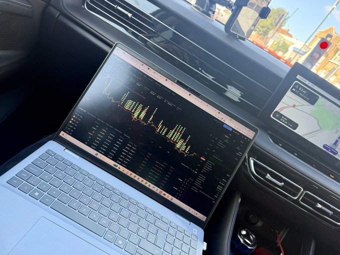A laptop displaying trading charts sits on the passenger seat of a car, with the Variational platform showing candlestick price action for a Lighter position next to the vehicle's built-in navigation screen. The setup visually reinforces the post's theme of grinding on the Variational trading platform while mobile, using Lighter's price action as motivation to chase triple-digit points in the remaining weeks of the competition.