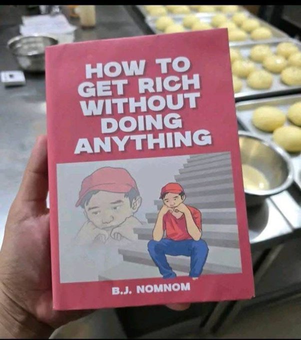A hand holds up a red book titled 'HOW TO GET RICH WITHOUT DOING ANYTHING' by 'B.J. NOMNOM', featuring an illustration of a bored boy in a red cap sitting on stairs, set against a bakery background with trays of dough.