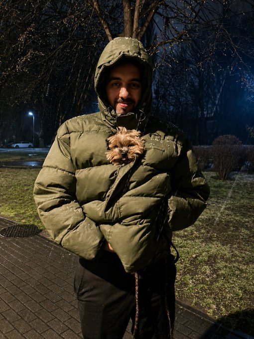 A person in a green puffer jacket holding a small Yorkshire terrier outdoors at night.