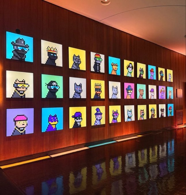 A modern interior hallway features a wall display of illuminated pixel-art character portraits, reflected in a dark, glossy floor below.