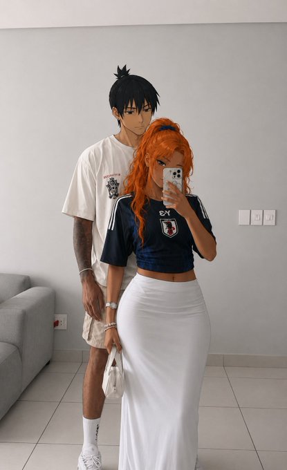 A couple takes a mirror selfie indoors, with the woman in a white maxi skirt and dark cropped jersey with vibrant orange hair, and the man in a white t-shirt and shorts behind her.