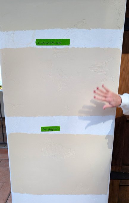 A person points toward a wall painted with beige and white stripes, each labeled with green painter's tape reading "Everlasting love" and "Happiness," symbolizing bullish "green candles" for XRP. The hand-drawn labels and green tape playfully evoke the optimistic sentiment of the XRP price prediction.