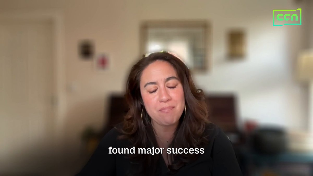 The image shows a woman sitting at a desk with her head resting on her hand while looking down. The background of the image features a white wall with a mirror hanging above it, as well as some pictures on the wall. There are also two books visible in the scene. The text "Found major success" is written below the woman's head and eyes, suggesting that she has achieved something significant or accomplished her goals.