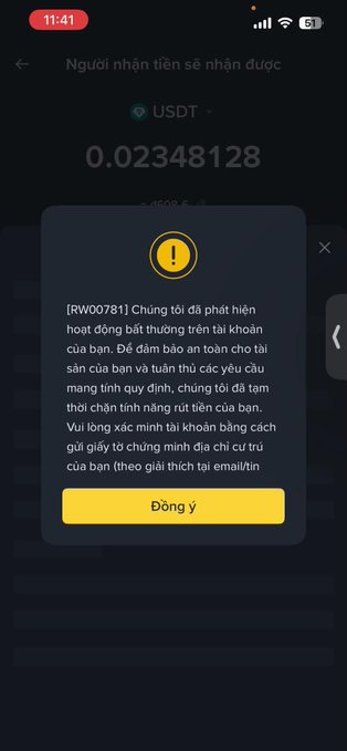 A mobile app screenshot showing a USDT balance of 0.02348128 with a warning popup in Vietnamese (RW00781) alerting the user to suspicious account activity.