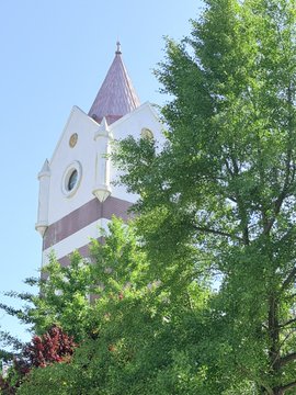 The image features a tall, white building with a pointed roof and a clock tower at its peak. The building is surrounded by lush green trees, creating a serene atmosphere. In the bottom right corner of the photo, there's a caption that reads "Thanks Crypto. Thanks #BNB". This suggests that someone might have taken this picture to capture the beauty of the scene or to share it on social media platforms.